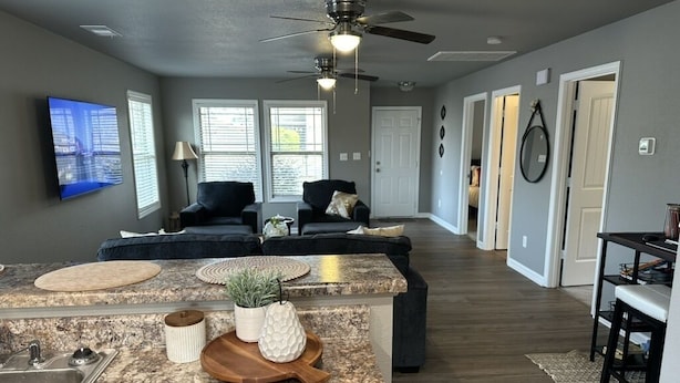 A modern living room with a large TV, a ceiling fan, and a kitchen area with granite countertops and a sink. - Cozy Corner <7 miles from Toyota Field and Redstone Arsenal - family-friendly! (Madison)
