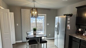 A compact kitchen with a refrigerator, a dining table with two chairs, and a hanging light fixture. - Cozy Corner <7 miles from Toyota Field and Redstone Arsenal - family-friendly! (Madison)