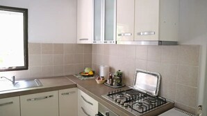 Une cuisine avec des meubles blancs, une cuisinière à gaz, un évier et une fenêtre.