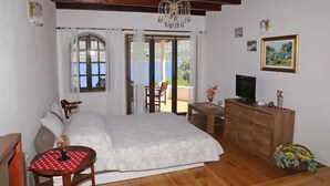 Une chambre à coucher avec un lit, une commode en bois, un téléviseur et une fenêtre avec des rideaux.