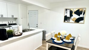 A modern kitchen with white cabinetry, a built-in stove, and a sink. There is a dining area with a table set for four, featuring a vase and napkins. -  Charming House in Old Town Fullerton near Disney & Knott’s!! (Fullerton)