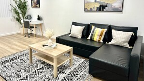 A modern living room with a black leather sofa, a wooden coffee table, a patterned rug, a white air conditioner, and a painting on the wall. -  Charming House in Old Town Fullerton near Disney & Knott’s!! (Fullerton)