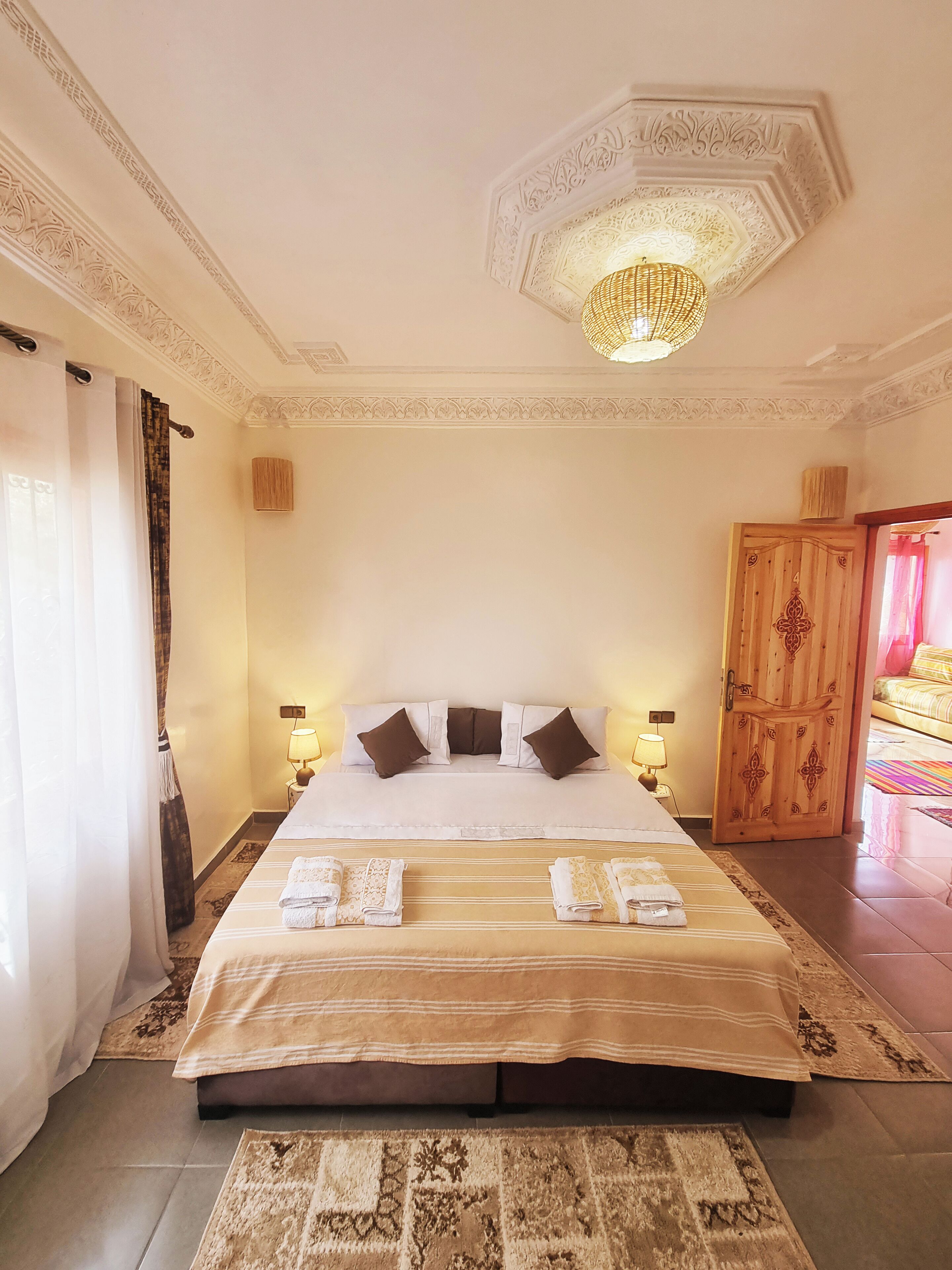 Une chambre d’hôtel avec un grand lit, deux lampes de chevet, un plafond décoratif et une porte en bois.
