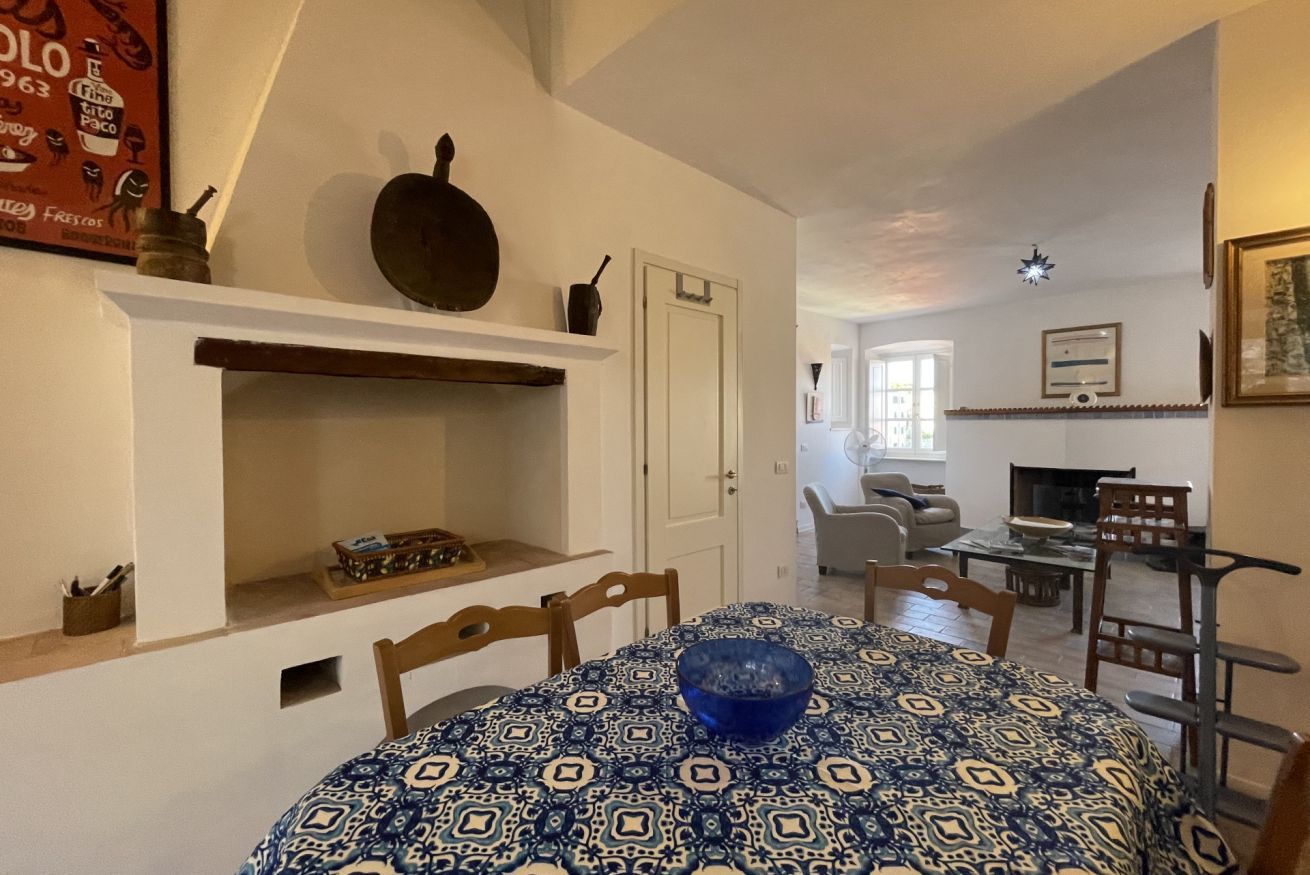 A dining area with a patterned tablecloth, a blue bowl, and a shelf with kitchen items.