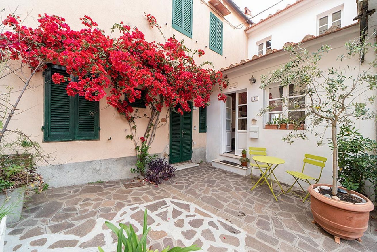 A courtyard with a stone floor, green shutters, and a potted plant.