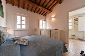 A bedroom with a bed, two windows, a radiator, a dresser, and a ceiling with wooden beams. - Villa Il Guardingo in Rio Elba (Rio Nell'Elba)