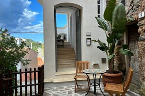 A courtyard with a stone floor, a wooden chair, a table, a potted plant, and a staircase leading to an upper level. - Villa Il Guardingo in Rio Elba (Rio Nell'Elba)