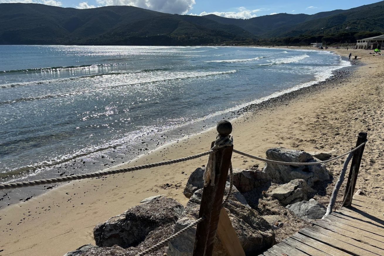 A beach with a wooden boardwalk, rocky outcrops, and a clear view of the ocean.