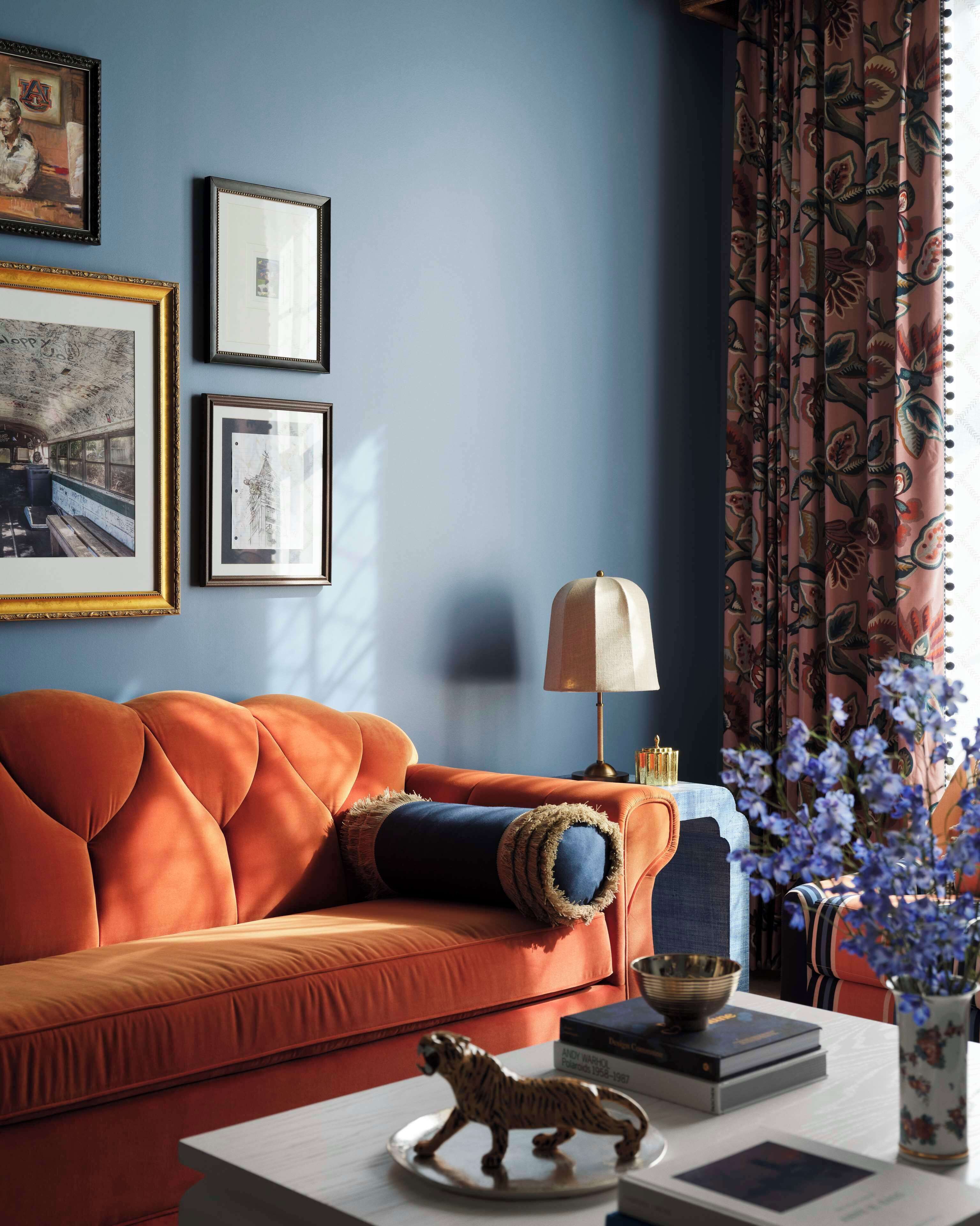 Quarto com parede azul, sofá, quadros emoldurados, abajur e uma estatueta de tigre decorativa.