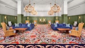 A spacious lobby with two blue sofas, wicker chairs, a patterned carpet, and a ceiling with a geometric design. - Graduate by Hilton Auburn AL (Auburn)