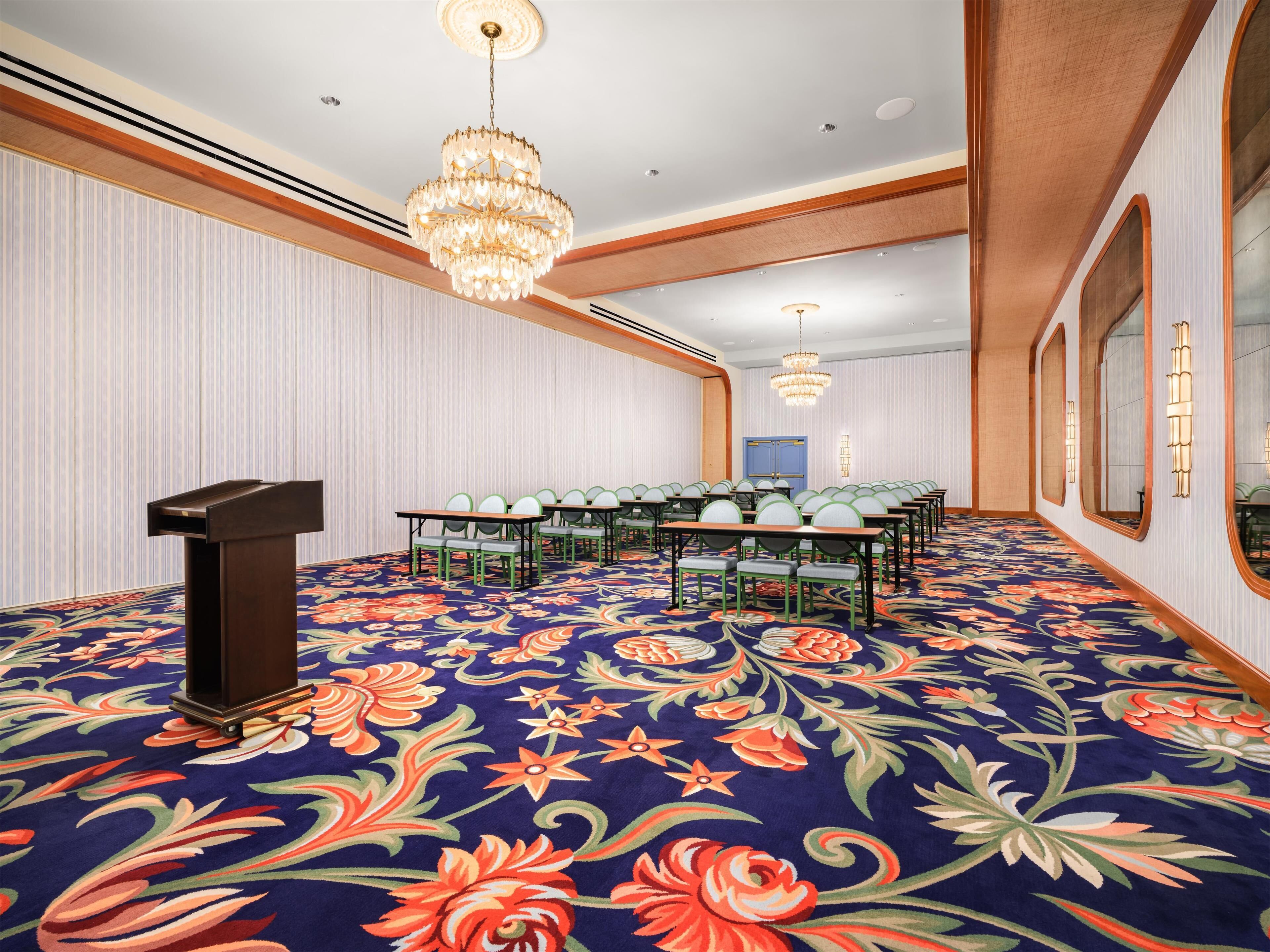 A conference room with a large floral carpet, a podium, and multiple rows of chairs.