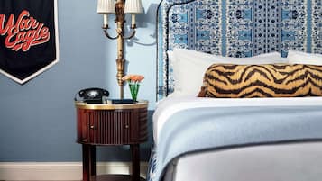 A bedroom with a blue patterned headboard, a decorative lamp, a framed 'War Eagle' sign, a vintage telephone, and a patterned rug.