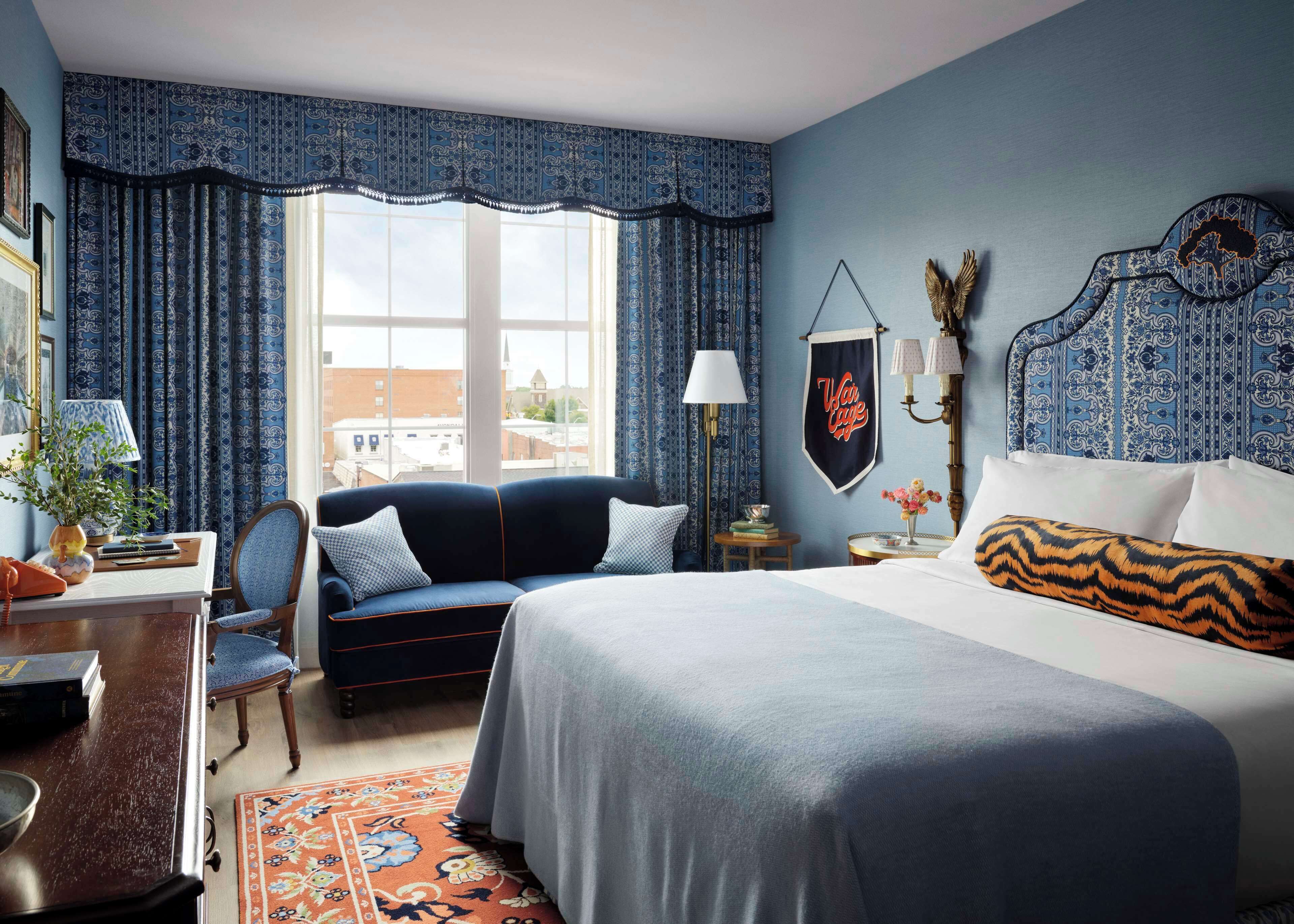 A hotel room with a large bed, a sofa, a desk with a lamp, and a view of the city.