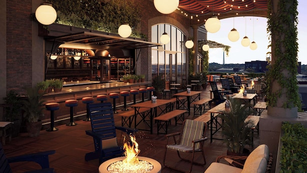 An outdoor bar area with wooden tables and chairs, a fire pit, and a bar counter with bottles. - Graduate by Hilton Auburn AL (Auburn)