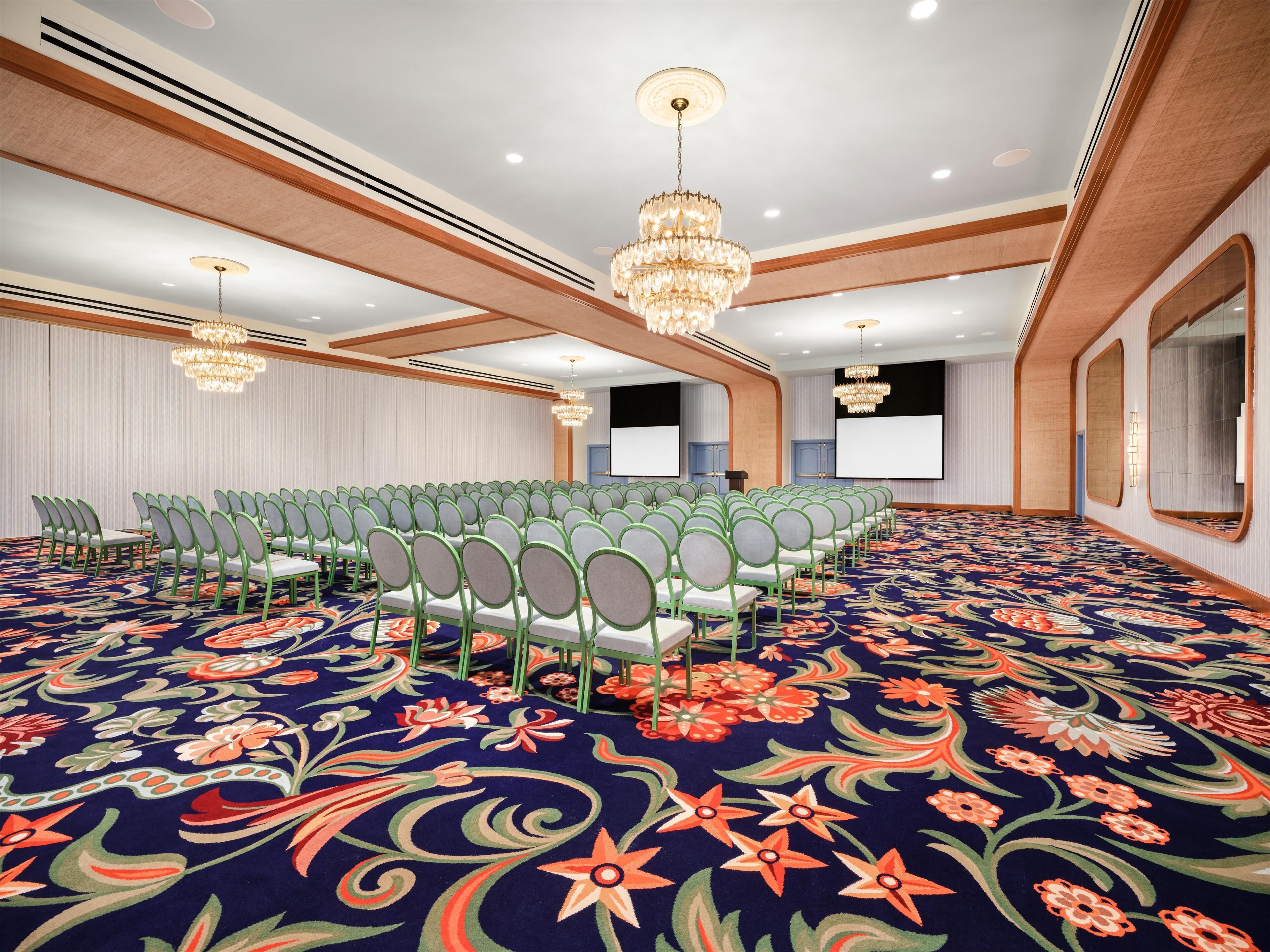 A conference room with rows of chairs, a large screen, and a chandelier.
