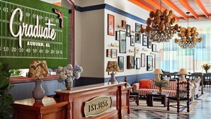 A hotel lobby with a football field wall, framed pictures, a chandelier, and a vintage reception desk. - Graduate by Hilton Auburn AL (Auburn)
