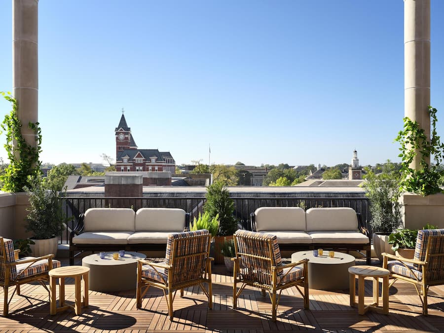 A rooftop terrace with a view of a historic building, furnished with wicker chairs and a sofa, and a wooden deck.