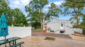 Un espace patio avec une table de pique-nique et un parasol, une clôture blanche et une maison avec un jardin devant.