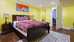 Une chambre à coucher comprenant un lit, des tables de chevet, une lampe, un tableau et une porte donnant sur une autre pièce.