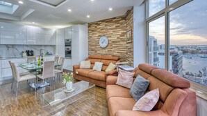A modern living room with a sofa, a dining table with chairs, and a large window overlooking a cityscape. - Roof terrace, Seaview 3 bedroom penthouse GOSLM-11 (Sliema)