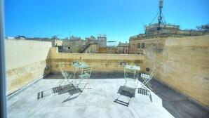 Una terraza en la azotea con dos mesas y sillas de metal, vistas despejadas del paisaje urbano y un edificio con antena parabólica.