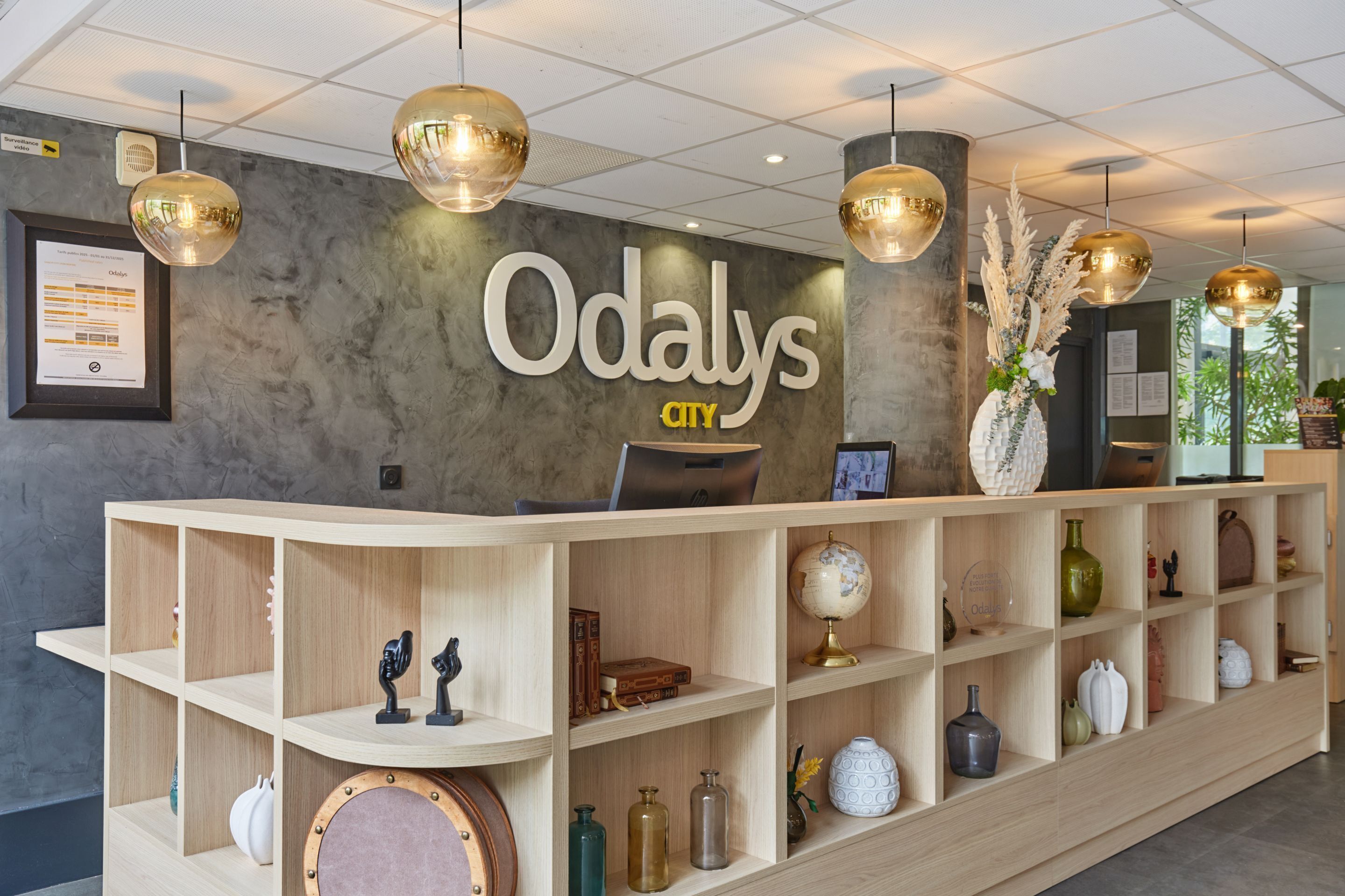 A reception desk with a sign reading "Odalys City" and a wooden shelving unit with various decorative items.