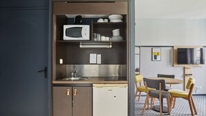 Eine kompakte Küchenzeile mit Mikrowelle, Spüle und kleinem Kühlschrank. Es gibt einen Essbereich mit rundem Tisch und Stühlen.