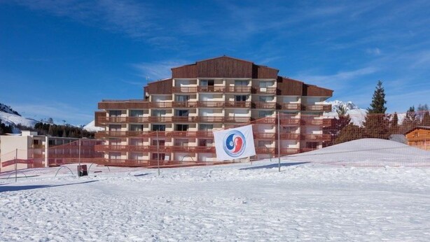 A multi-story hotel with a modern architectural design, featuring balconies and a ski slope in the background.