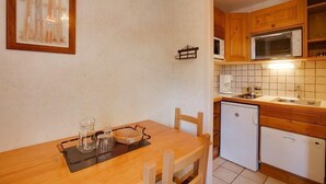 A compact kitchen with wooden cabinets, a microwave, a small refrigerator, and a dining table with chairs.