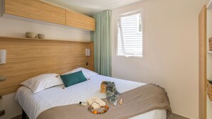 A bedroom with a wooden headboard, a bed with white bedding, a green pillow, and a window with blinds.