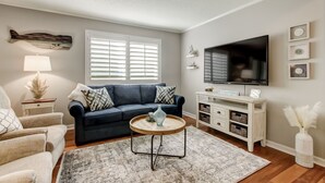Ein Wohnzimmer mit einem dunkelblauen Sofa, einem runden Couchtisch, einem Fernseher und einer weißen Kommode.