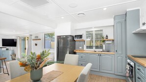 Une cuisine moderne avec des armoires grises, un four à micro-ondes encastré et un réfrigérateur. On y trouve un coin repas avec une table et des chaises, ainsi qu’une plante posée sur la table.