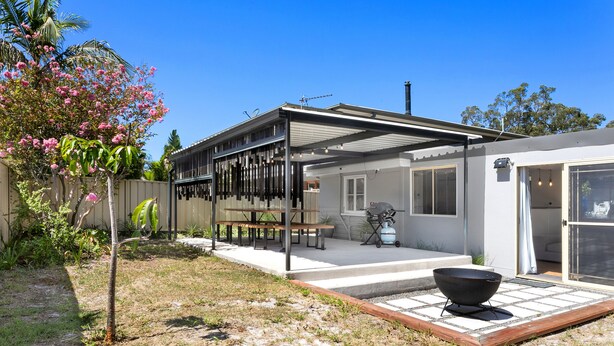 Een modern huis met een overdekte patio, een barbecue en een tuin met bloeiende planten.