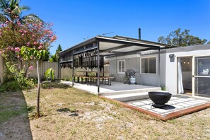 A modern house with a covered patio, a barbecue grill, and a garden with flowering plants. - Spitaki (Nelson Bay)
