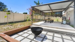 Een overdekt terras met een barbecue, een tafel en stoelen.