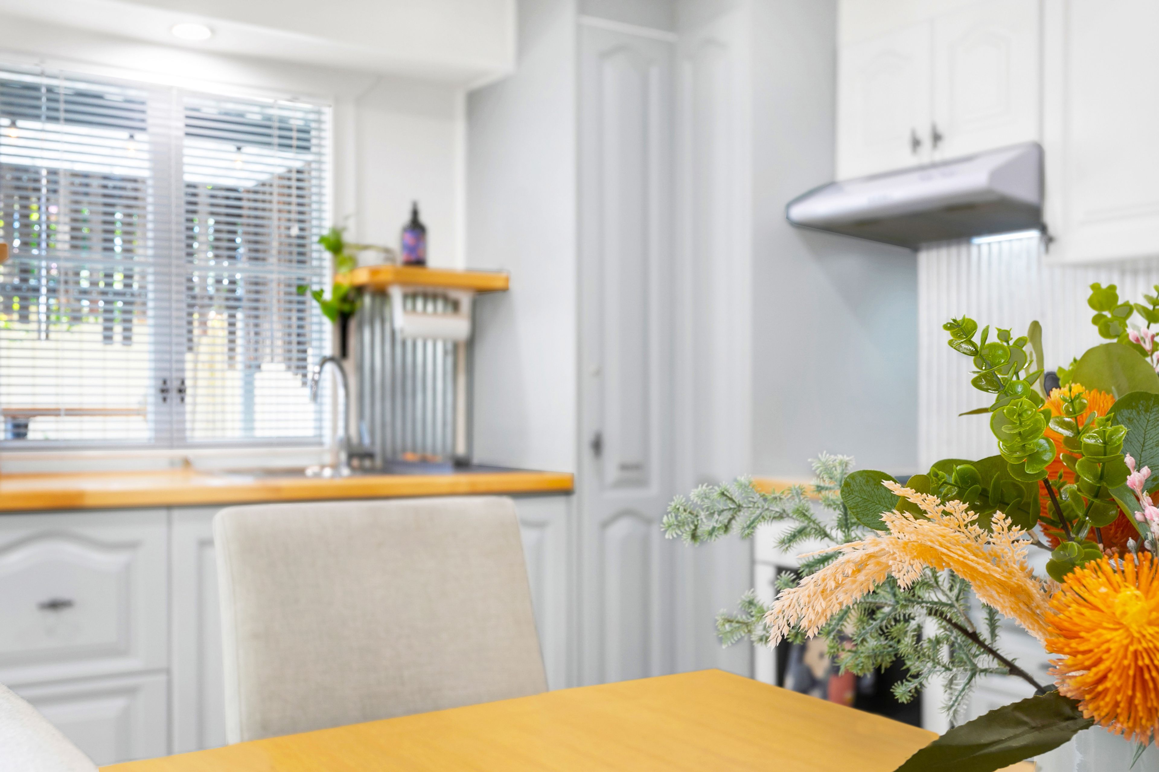 A modern kitchen with white cabinetry, a window with blinds, and a dining area with a yellow table.