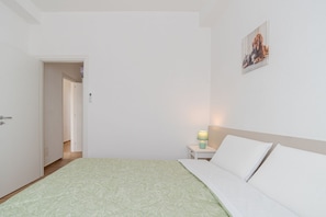 A bedroom with a bed, a nightstand with a lamp, a door, and a wall-mounted picture.
