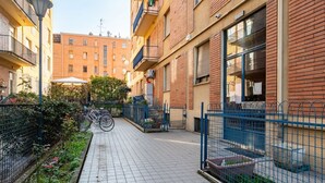 A narrow urban alleyway with tiled flooring, a blue metal fence, and a row of buildings with balconies and windows. - GuestHost - Comfortable apartment located on the mezzanine floor of a building, with five floors in total, from the 70s. There are steps to access it (NO lift).In 85 m2 of space it accommodates 5 guests.We are in a very lively neighborhood, where the cit (Parma)