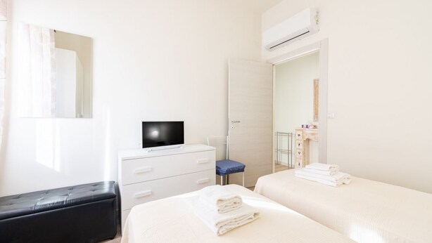 A hotel room with two beds, a TV, a wardrobe, and an air conditioning unit. - GuestHost - Comfortable apartment located on the mezzanine floor of a building, with five floors in total, from the 70s. There are steps to access it (NO lift).In 85 m2 of space it accommodates 5 guests.We are in a very lively neighborhood, where the cit (Parma)