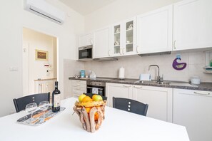 Una cucina moderna con mobili bianchi, un forno a microonde e un lavello. Sul tavolo c'è un cesto di frutta con arance e limoni.