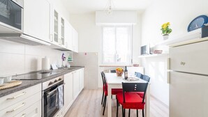 A modern kitchen with white cabinets, a built-in oven, a dining table with red chairs, and a refrigerator. - GuestHost - Comfortable apartment located on the mezzanine floor of a building, with five floors in total, from the 70s. There are steps to access it (NO lift).In 85 m2 of space it accommodates 5 guests.We are in a very lively neighborhood, where the cit (Parma)