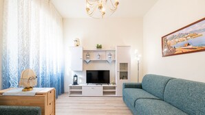 A living room with a TV, sofa, and decorative items. - GuestHost - Comfortable apartment located on the mezzanine floor of a building, with five floors in total, from the 70s. There are steps to access it (NO lift).In 85 m2 of space it accommodates 5 guests.We are in a very lively neighborhood, where the cit (Parma)