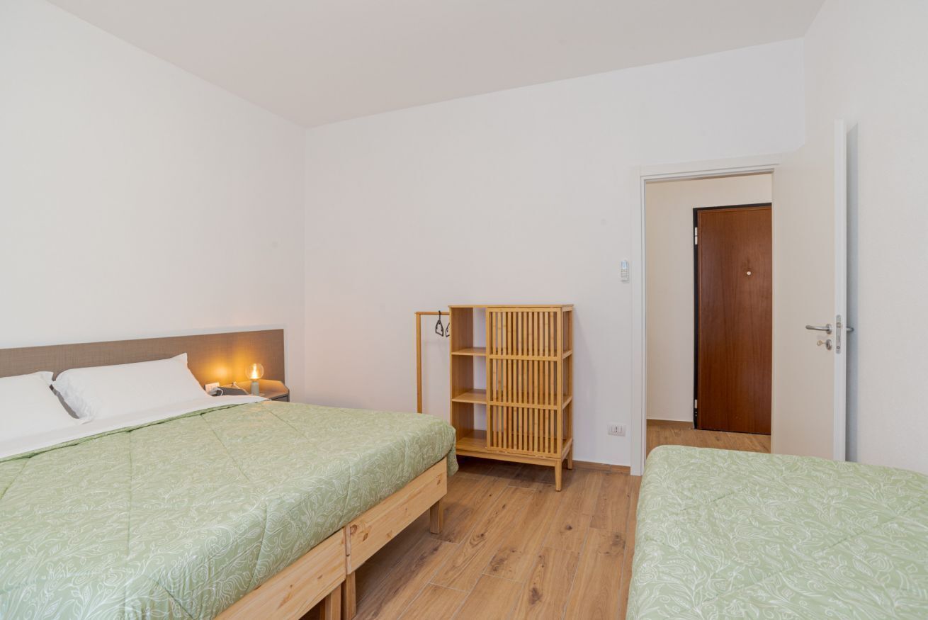Une chambre avec deux lits, une armoire en bois, une table de chevet avec une lampe et une porte.