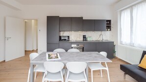A modern kitchen with grey cabinets, a marble backsplash, and a dining area with a grey table and white chairs.