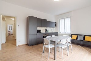 A modern kitchen with grey cabinets, a dining table with chairs, and a sofa with cushions.