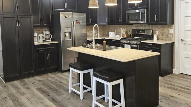 A modern kitchen with dark cabinets, a central island with stools, stainless steel appliances, and pendant lighting. - Lake Cabin, Fishing Access, swimming, walk to lake, boat parking, fenced yard!  (Nancy)
