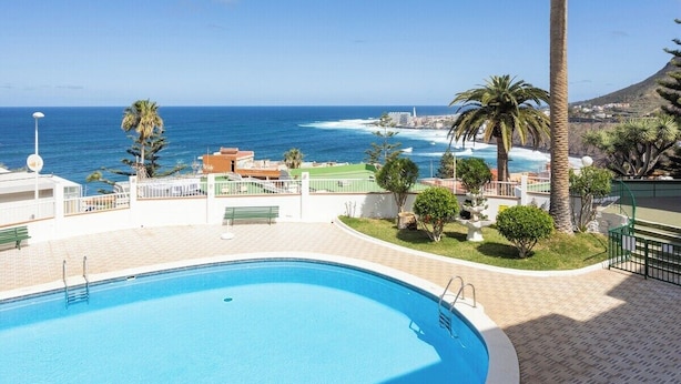 A swimming pool with a view of the sea and palm trees. - Home2Book Bright Sea Views Apartment & Pool (Bajamar)