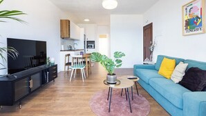 A modern living room with a sofa, a TV, a dining area, and a kitchen in the background. - Home2Book Bright Sea Views Apartment & Pool (Bajamar)