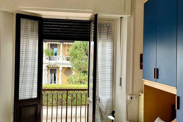 Puerta abierta a un balcón con vista a un edificio y follaje verde.