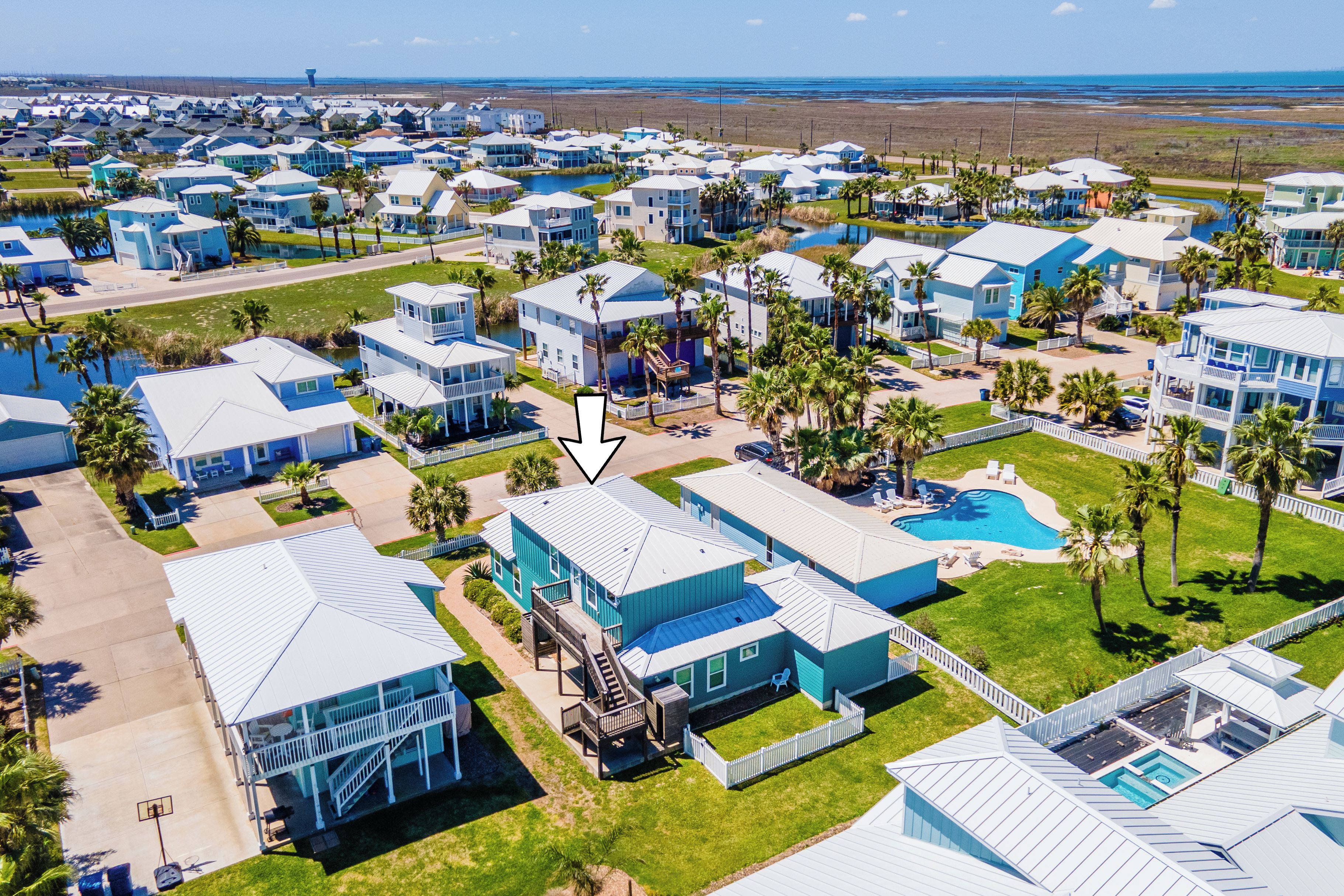 A coastal residential area with multiple blue houses, a central swimming pool, and a staircase leading to a covered area.